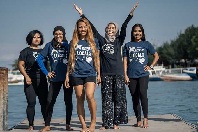 5 vrouwen staan in de buurt van het water, met een glimlach - het dragen van shirts met zeedieren en de woorden Respect Locals