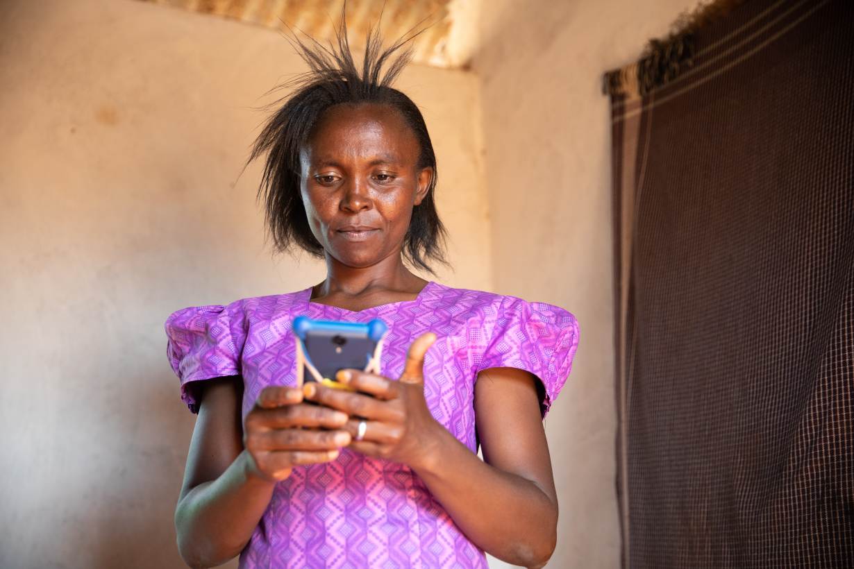 Een Keniaanse vrouw in een paarse jurk gebruikt haar mobiele telefoon