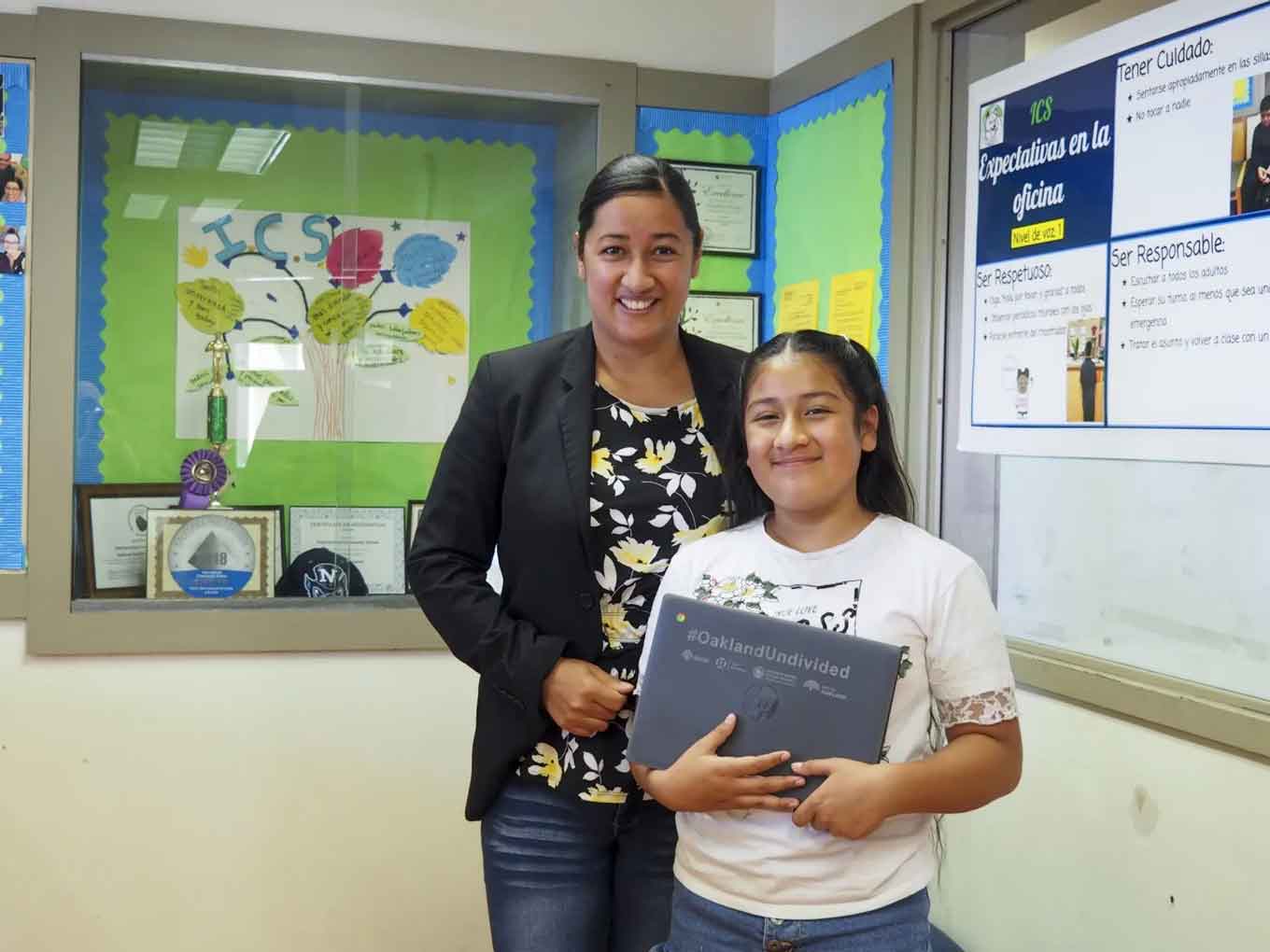 Maria G. Islas, een medewerker van Think College Now, een openbare basisschool in Oakland, met haar dochter, Jesimiel Merida-Islas, die een laptop en hotspot kreeg na maanden van het delen van een computer met haar moeder.