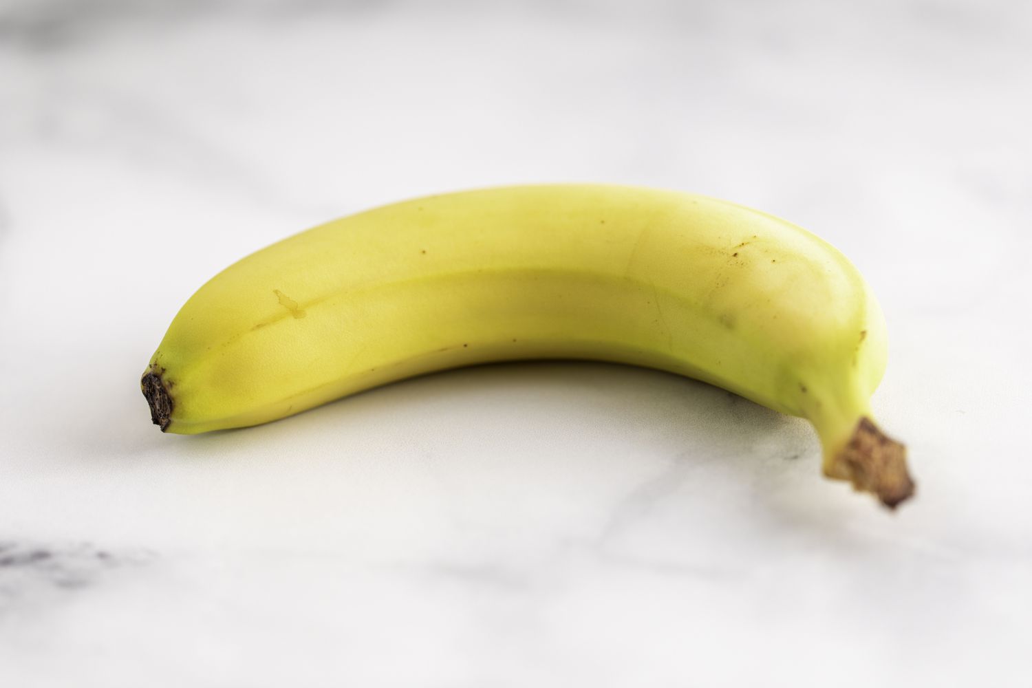 Een enkele banaan op een marmeren oppervlak.