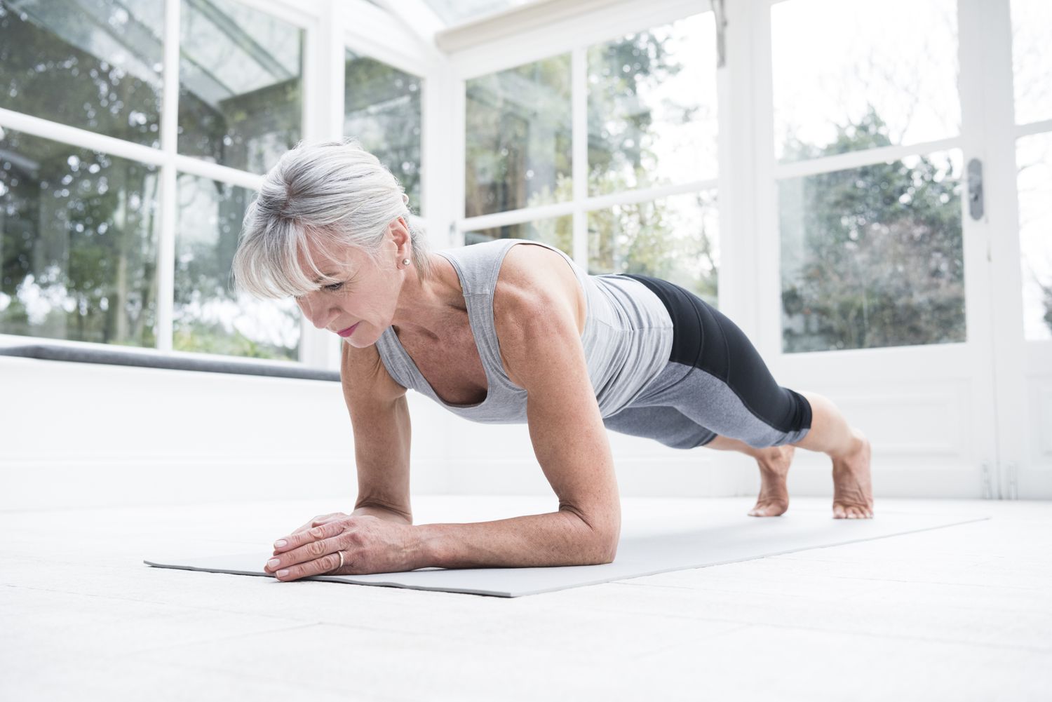 Oudere vrouw die een plank op een yogamat doet