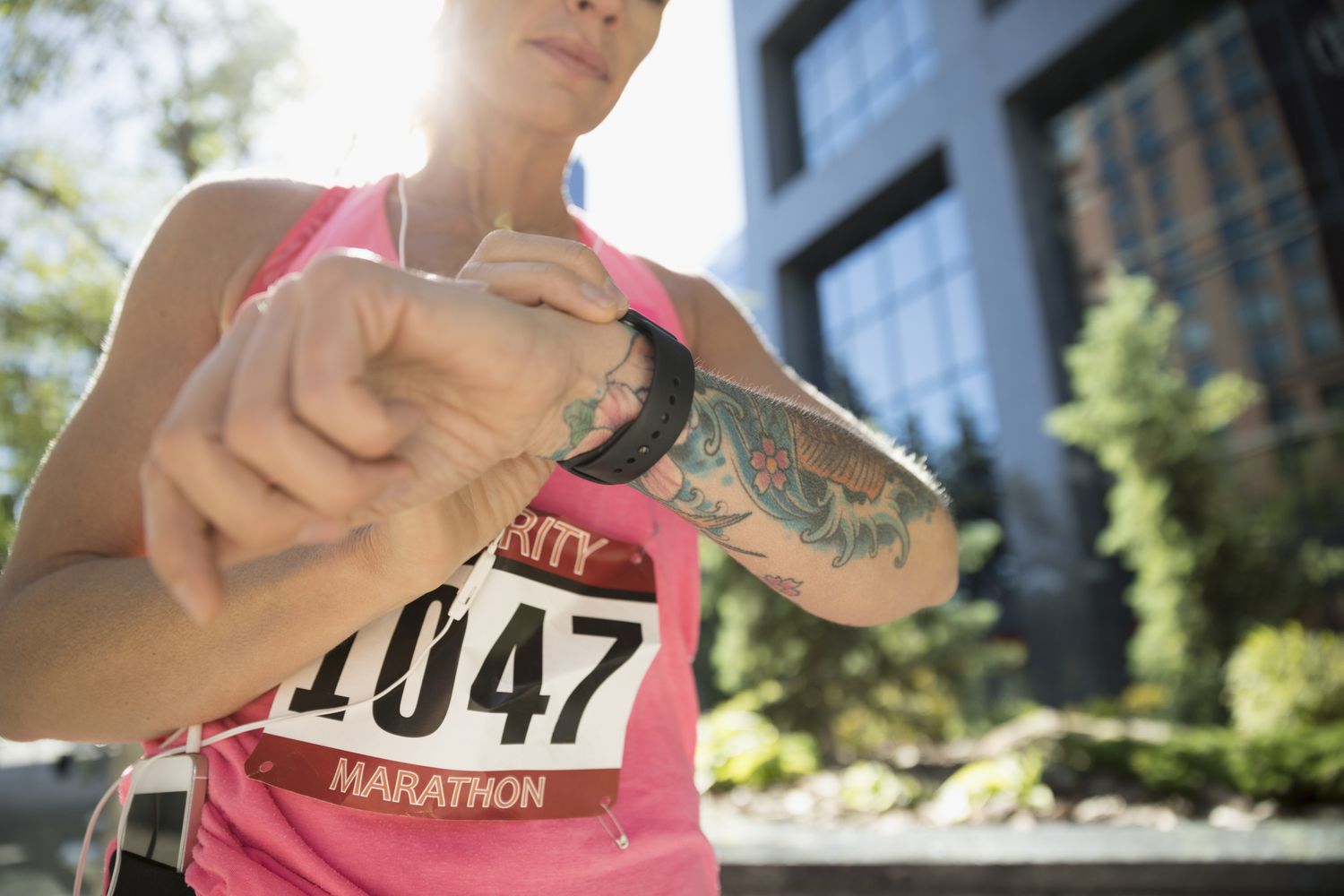 Getatoeëerde vrouwelijke marathonloper die slim horloge controleert in stadspark